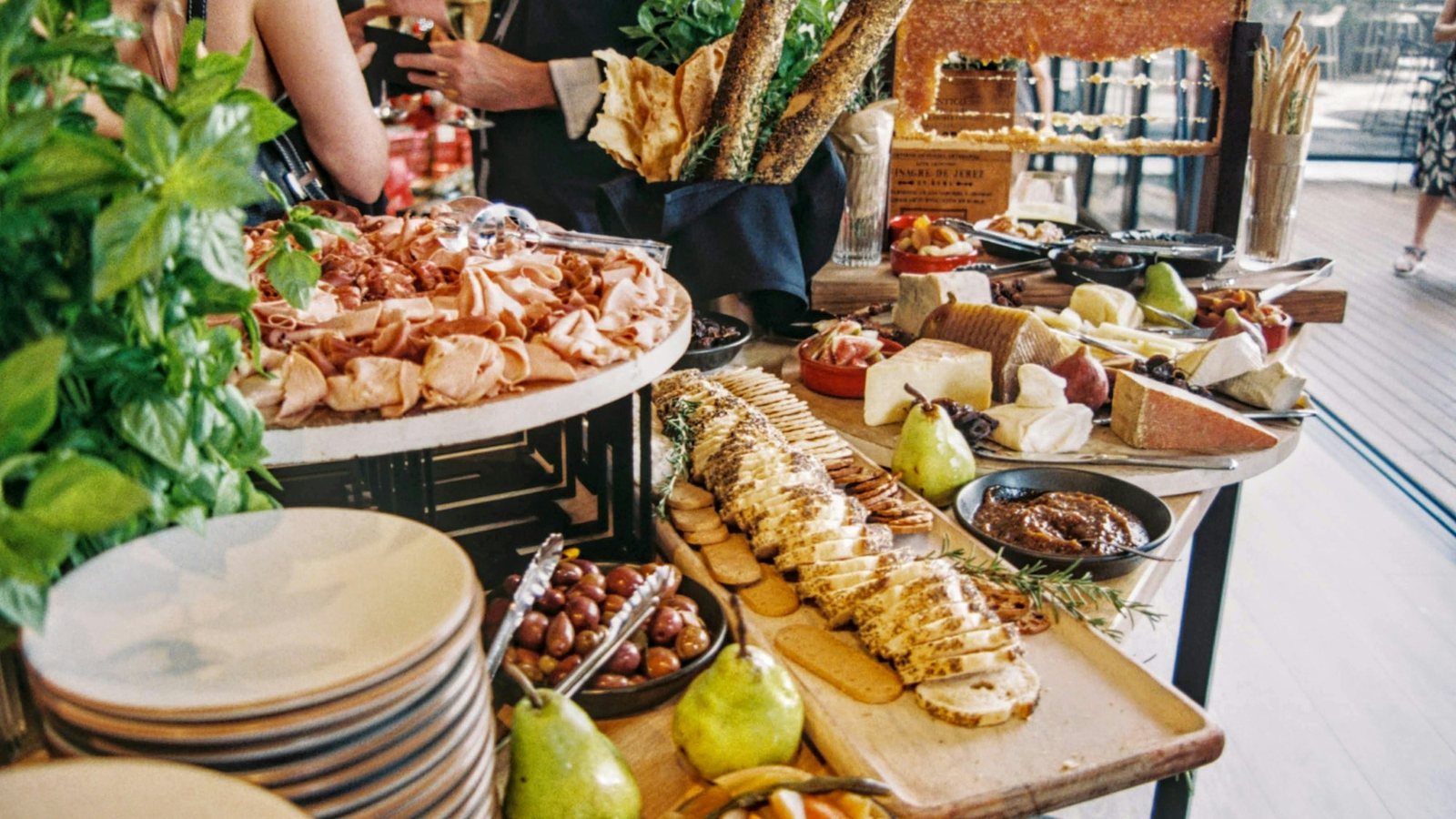 Guests serving themselves from a catering spread of cured meats, cheeses, bread and fruit at an event